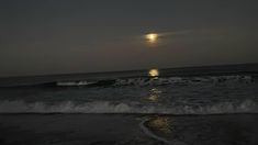 the moon is setting over the ocean with waves