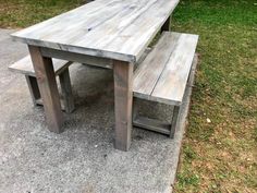 a wooden table and bench sitting on the side of a road in front of some grass