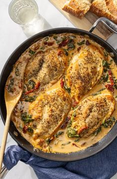 chicken with spinach and cheese in a skillet on a table next to bread