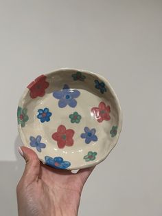 a hand holding a bowl with flowers painted on the bottom and sides, in front of a white wall