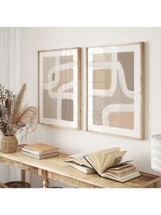 two framed art prints on the wall above a table with books and flowers in vases