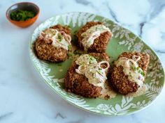 four crab cakes on a green plate with white sauce and garnishes next to a small bowl