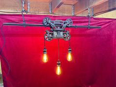 three light bulbs are hanging from the ceiling in front of a red cloth covered wall