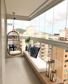 a balcony with a swing chair and pillows on the floor next to a large window