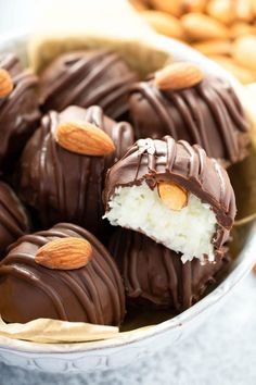 chocolate covered almonds in a bowl with nuts on the side and one half eaten