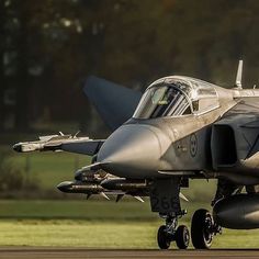 a fighter jet sitting on top of an airport tarmac with grass in the background