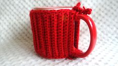 a crocheted red coffee mug holder on a white blanket with a handle and handles