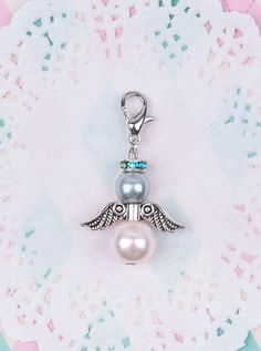 a silver charm with a pearl and angel wings on it's side, sitting on top of a doily