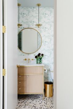 a bathroom with a sink, mirror and gold accents on the wall above it is an open door that leads to another room