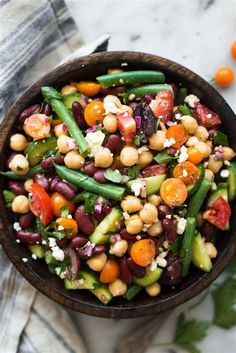 a wooden bowl filled with beans and veggies on top of a white table