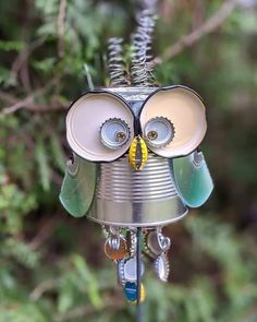 a tin can owl ornament hanging from a tree branch with its eyes open