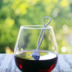 a wine glass filled with red wine sitting on top of a table next to a heart shaped bottle opener