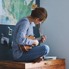 a woman sitting on top of a wooden table playing a guitar