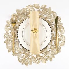 a white plate topped with a gold napkin next to a golden fork and knife set on top of it