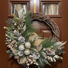 a wreath on the front door with pine cones and evergreens hanging from it's side