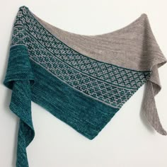 a knitted shawl hanging on the wall with a blue and grey scarf draped over it