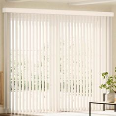 a living room with white vertical blinds on the windowsills and a table in front of it