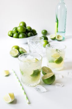 three glasses filled with water and lemons on top of a wooden table next to green leaves