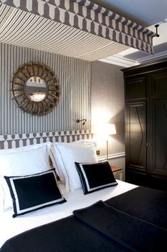 a bed with white sheets and black pillows in a room that has striped wallpaper on the walls