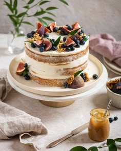 there is a cake on the table with figs and blueberries on it, next to a glass of orange juice