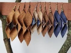 several pairs of earrings hanging from a tree branch in front of a white wall with brown and blue leaves on it