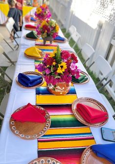 a long table with colorful plates and napkins on it, along with flower centerpieces