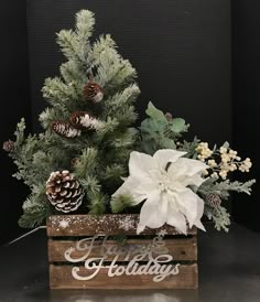 a wooden box filled with pine cones and white flowers next to a small christmas tree