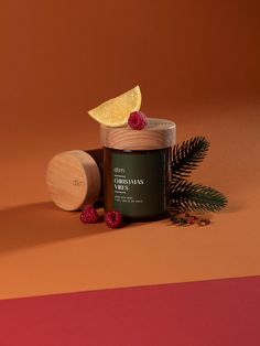 a jar of lemon and raspberry body scrub next to a pine cone on an orange background