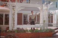 a man standing in front of a white pergolan on a porch next to a house