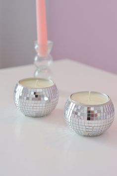 two silver candles sitting next to each other on a white table with a pink candle