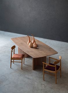 a wooden table with two chairs and vases on it, in front of a gray wall