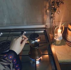 a person is cooking on the stove with a tea pot in front of them and some candles