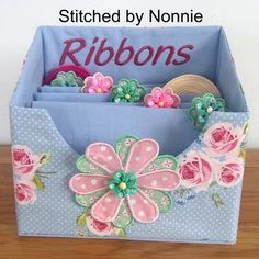 a blue fabric box with pink flowers and personalized name on the front, sitting on a wooden table