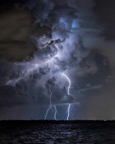 a large cloud filled with lots of lightning above the ocean in front of dark clouds