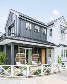 two wicker chairs sit on the front porch of a modern house with white picket fence