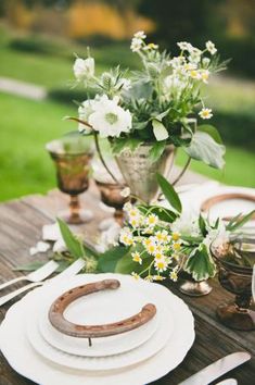 the table is set with white plates, silverware and vases filled with flowers