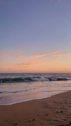 a person walking on the beach with a surfboard in their hand, at sunset