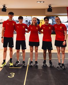 four people in red shirts and black shorts standing on a basketball court