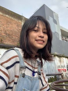 a woman standing in front of a building with her eyes closed and wearing overalls