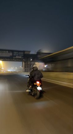 a person riding a motorcycle on a highway at night time with lights in the background