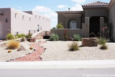 a house in the desert with rocks and plants on the front lawn, along with other houses