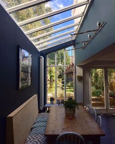 a wooden table sitting under a glass roof in a room with blue walls and windows