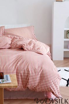 a bed with red and white gingham sheets on it, next to a small table