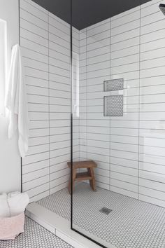 a white tiled bathroom with a wooden bench in the corner and shower stall door open