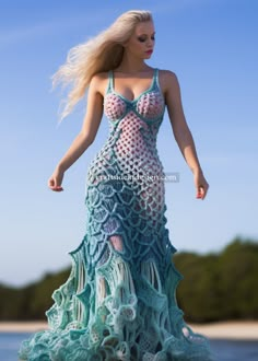 a woman in a crocheted dress is walking on the beach with her hair blowing in the wind