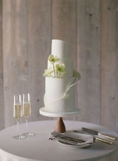 a white wedding cake sitting on top of a table next to two glasses of wine