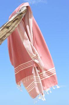 a pink and white towel hanging from a wooden pole on the beach under a blue sky