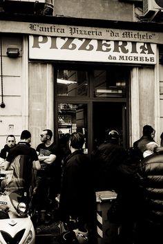 black and white photograph of people standing in front of a pizza shop