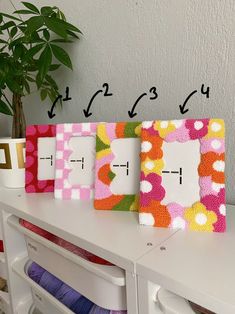 three frames with different designs on them sitting on top of a white table next to a potted plant