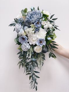 a bouquet of white and blue flowers is held up by someone's hand against a wall